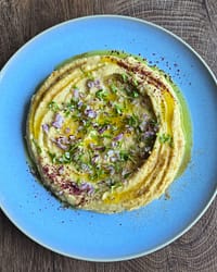 Angerichtetes Fava auf blauem Teller mit Olivenöl, Petersilie und roten Zwiebeln.