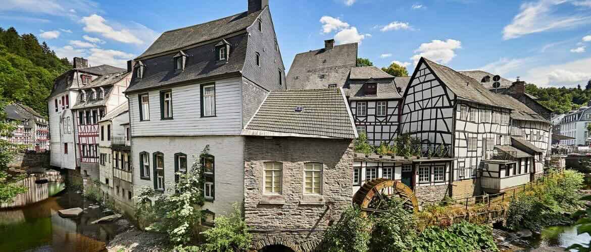 Fachwerkhäuser und eine historische Wassermühle in einer malerischen Altstadt am Flussufer.