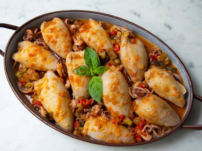 Gefüllte Kalamari, Greek Cuisine Magazine Gefüllte Kalamari mit Reis und Kräutern, angerichtet in einer Keramikschale – ein traditionelles Gericht der griechischen Küche.